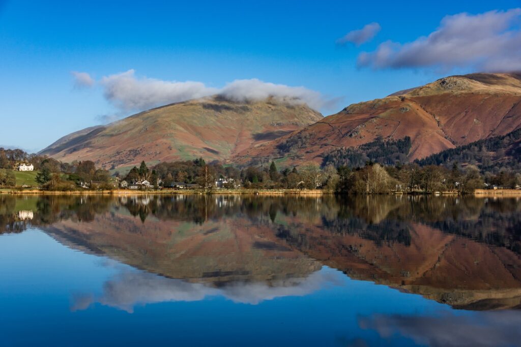 brown and green mountain beside lake under blue sky during daytime